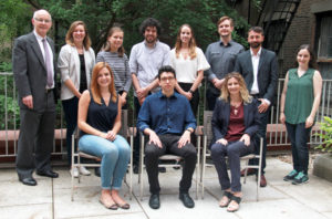 Picture of the IILJ Members. Three members are sitting in chairs while the rest of them stand in a row behind them.